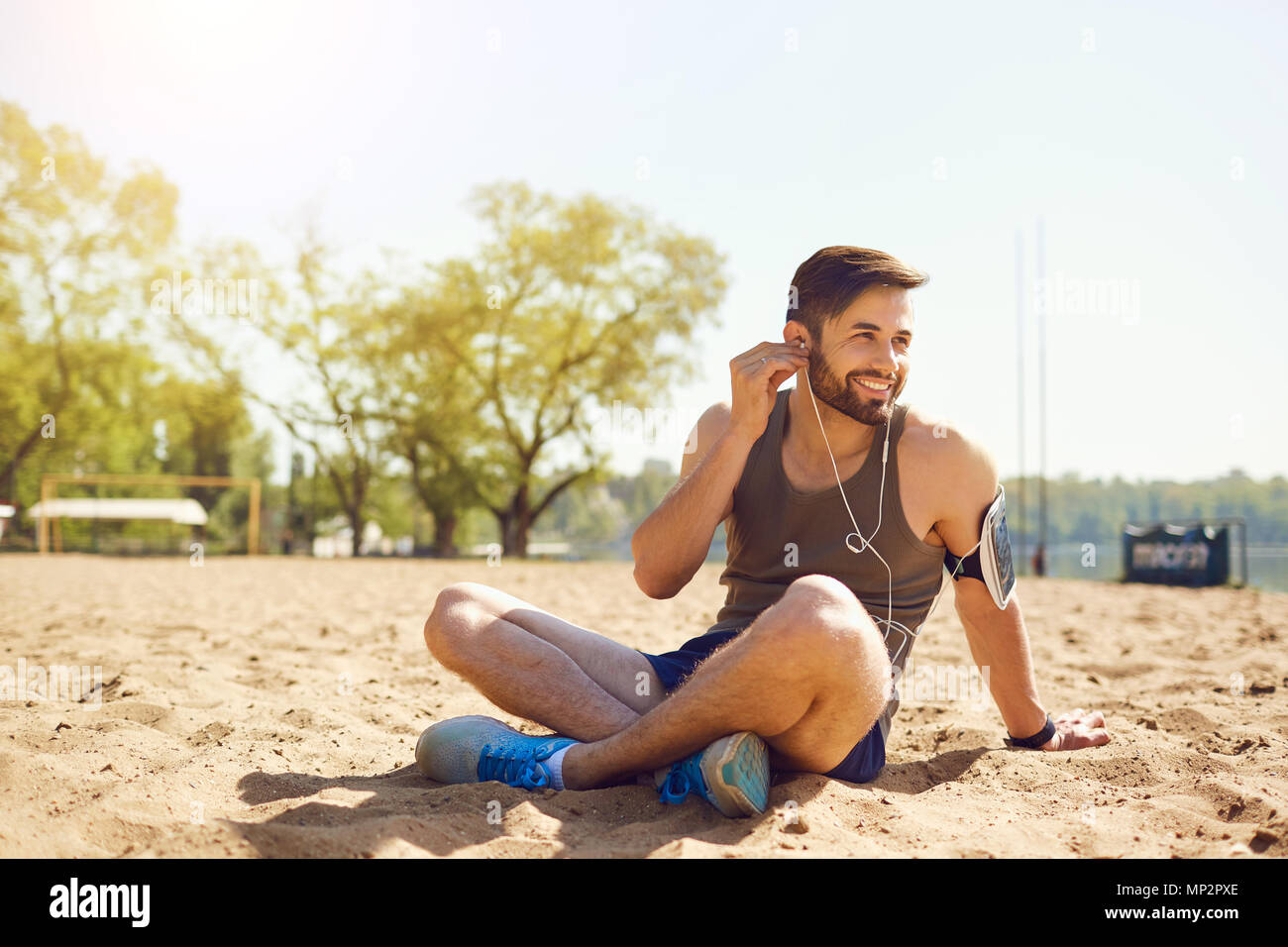 Ein bärtiger Sportsman sitzt auf dem Sand am Strand. Stockfoto
