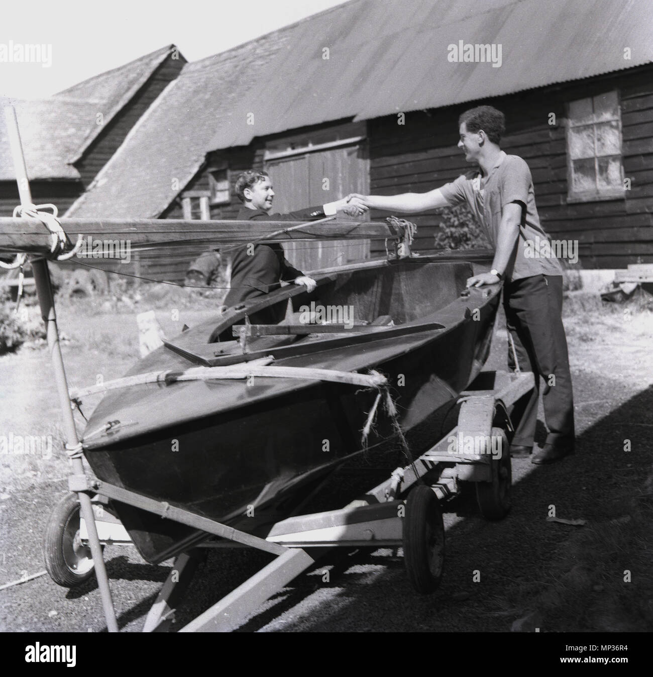 1964, historische,.." Sein Ihr'....Mann die Hände schütteln und Übergabe einer kleinen offenen Boot oder Beiboot, mit Mast und Segel, einer jungen Person, "England, UK. Stockfoto