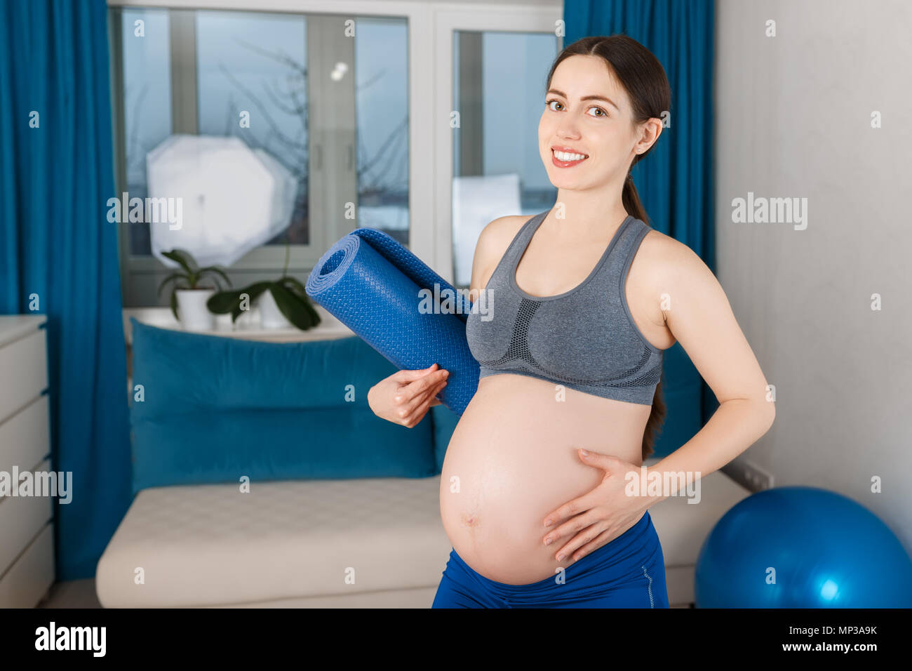 Portrait der schwangeren Frau mit blauen Yoga Matte. Die werdende Mutter ihr Bauch berühren nach Gymnastik zu Hause Stockfoto