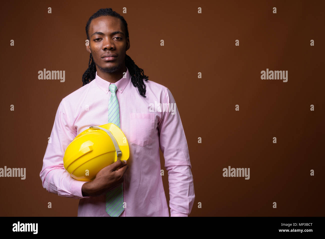 Jungen schönen afrikanischen Geschäftsmann mit hardhat gegen Braune ba Stockfoto