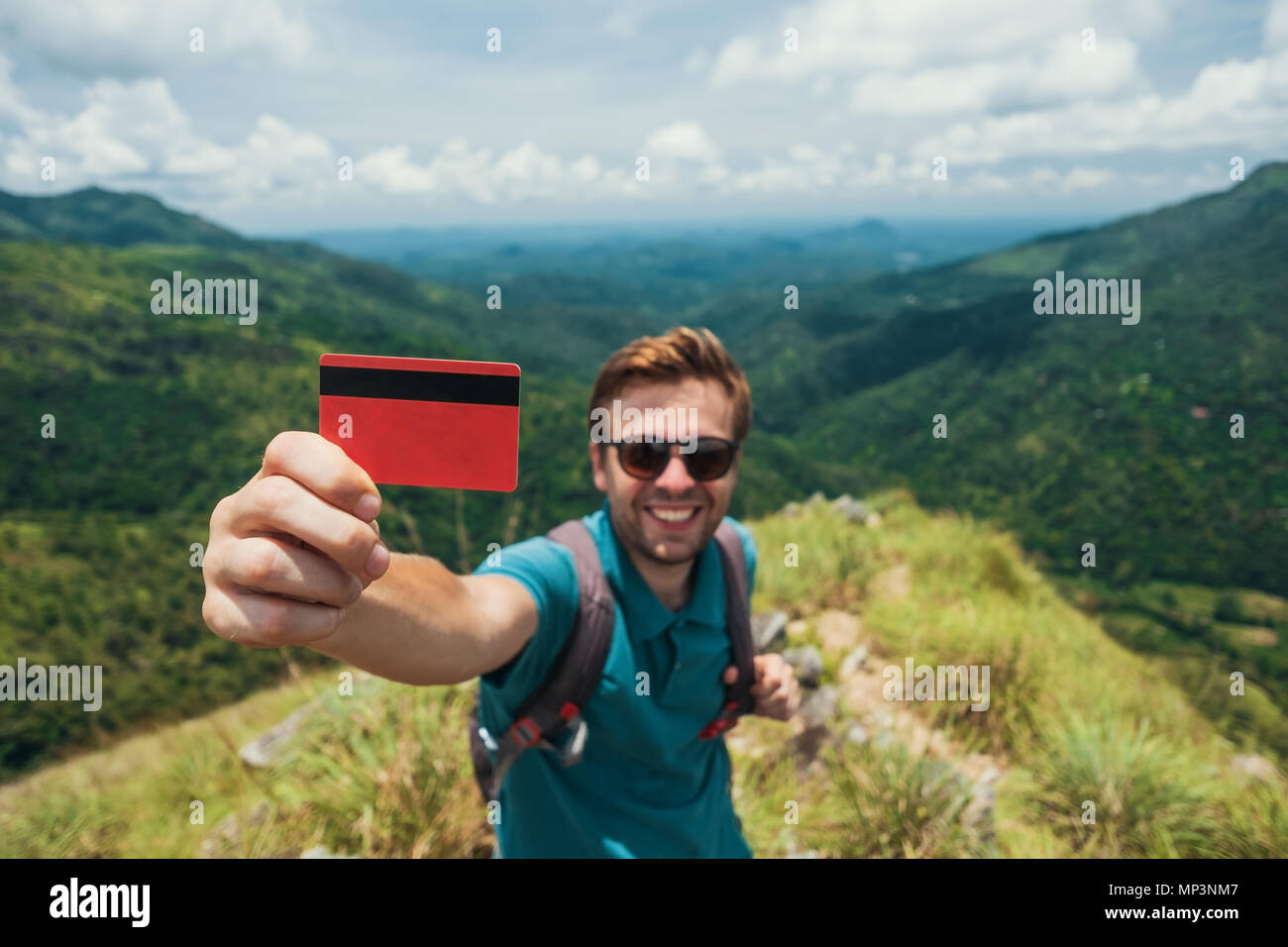Junge lächelnde Mann zeigt leere Kreditkarte. Er steht an der Spitze des Berges und zeigt die outdoor Schönheit. Stockfoto
