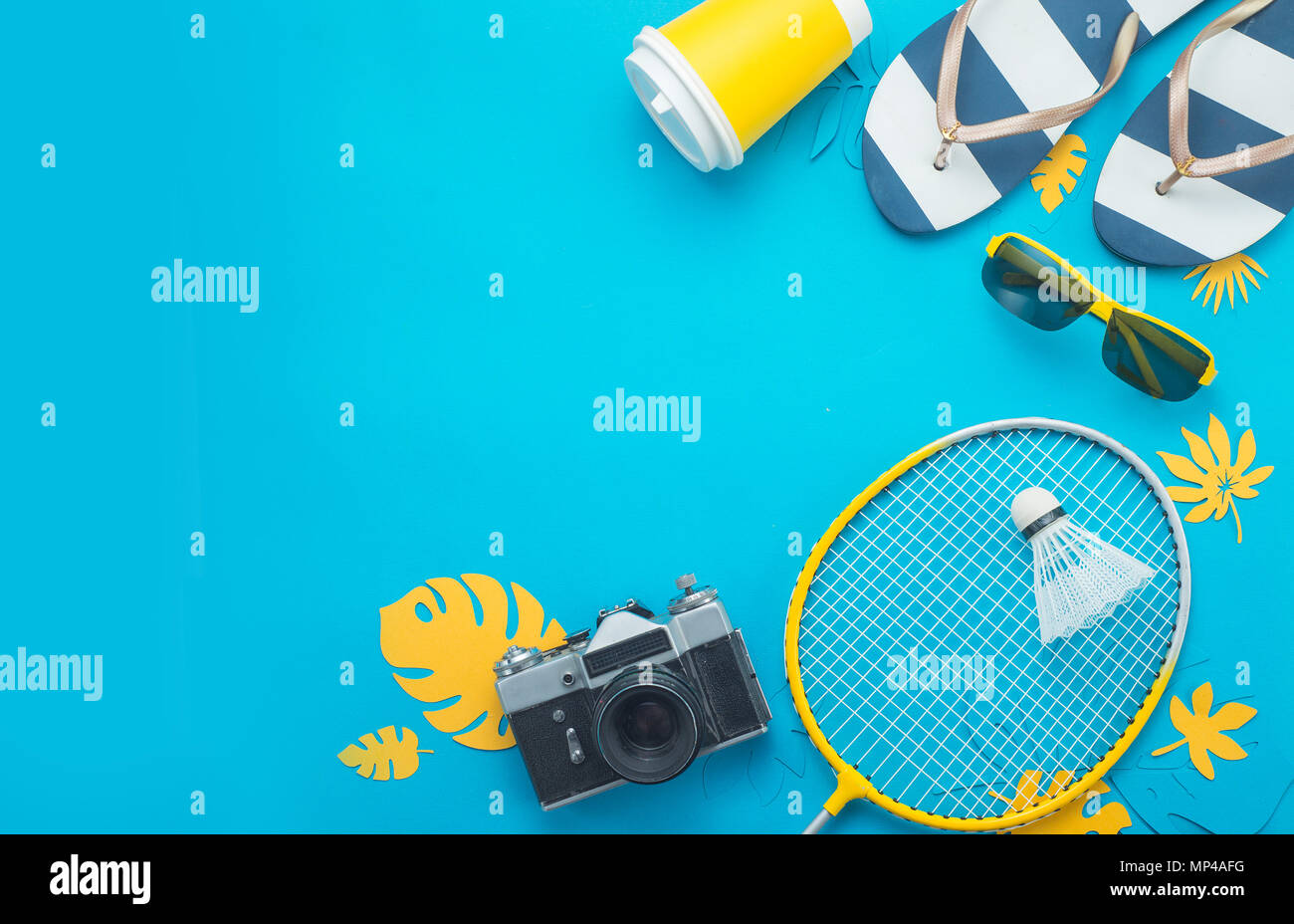 Aktivitäten im Sommer. Badminton Rakete mit tropischen Blättern, Flip Flops, Sonnenbrille, Sonnencreme, Kamera und Papier Schale von oben auf ein helles Blau b Stockfoto