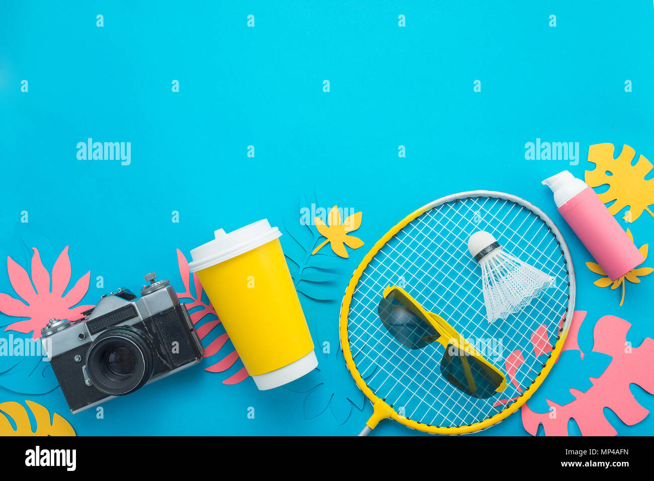 Aktivitäten im Sommer. Badminton Rakete mit tropischen Blättern, Flip Flops, Sonnenbrille, Sonnencreme, Kamera und Papier Schale von oben auf ein helles Blau b Stockfoto