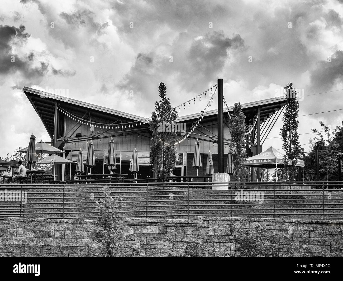 Kunden sitzen unter Sonnenschirmen, vor dramatische Wolken, außerhalb der Verkostung Zimmer im New Belgium Brewing Company in Asheville, NC, USA Stockfoto