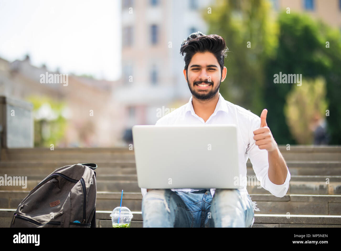Happy Indischer Student sitzt auf der Treppe Daumen zeigt, Arbeiten am Laptop, auf dem Campus der Universität. Stockfoto