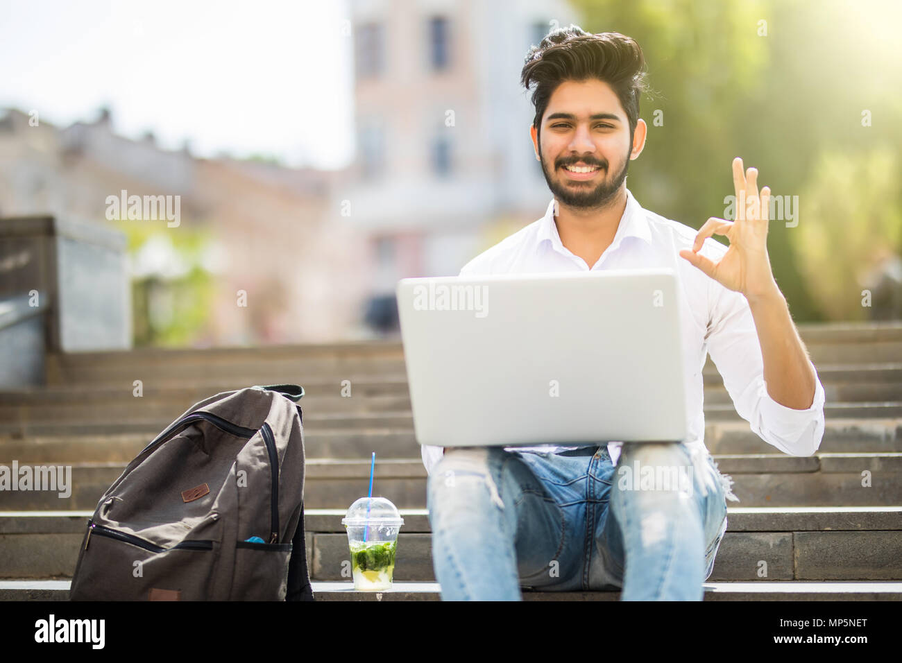 Happy Indischer Student sitzt auf der Treppe, okay Zeichen Arbeiten am Laptop, auf dem Campus der Universität. Stockfoto