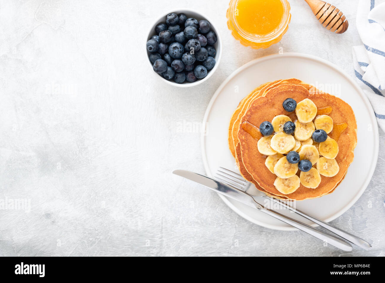 Buttermilch Pfannkuchen mit Banane, Blaubeeren und Honig auf konkreten Hintergrund. Ansicht von oben und kopieren Sie Platz für Text. Blick von oben auf die Pfannkuchen mit Beeren auf Stockfoto