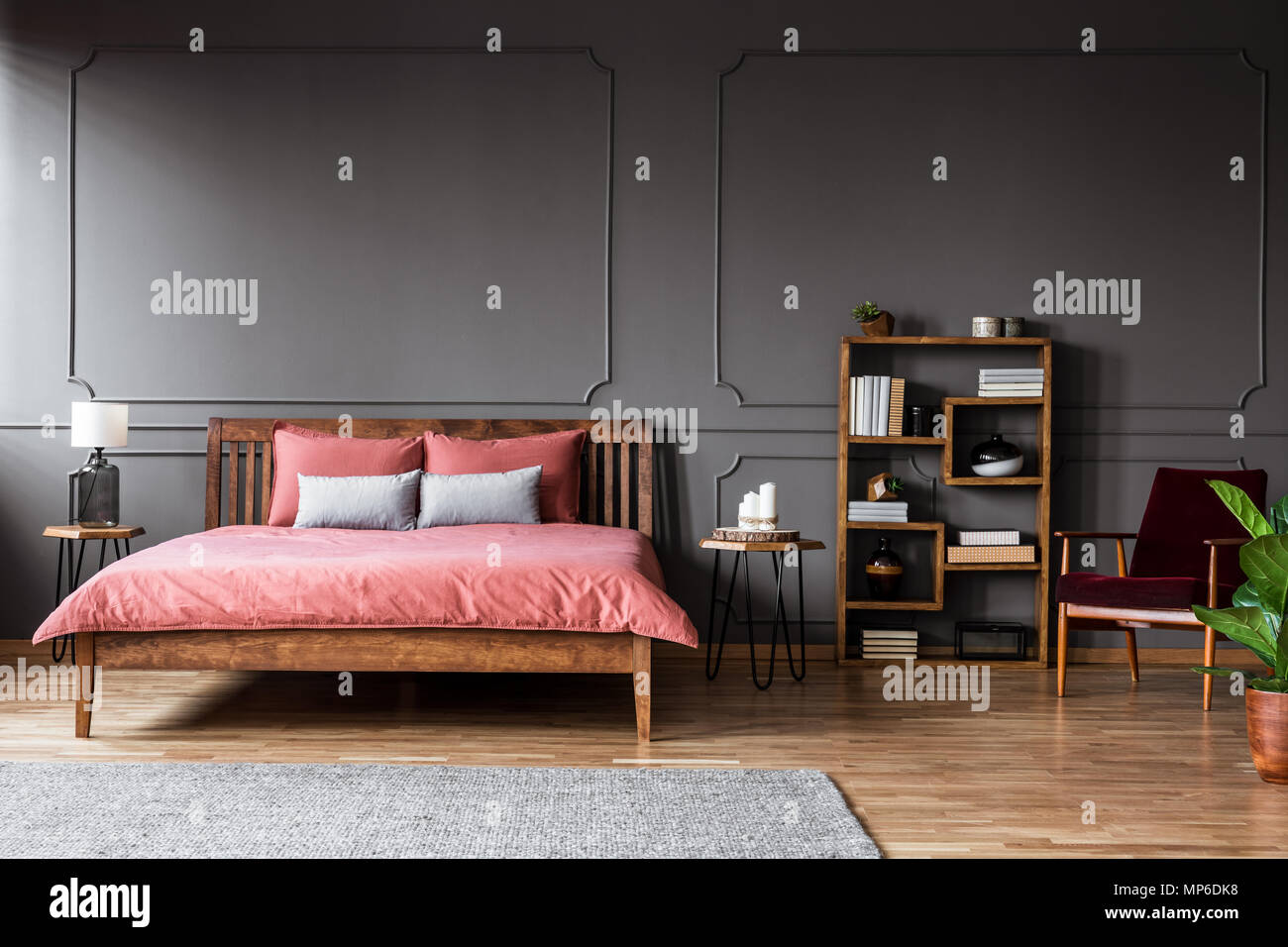 Real Photo von einem geräumigen Schlafzimmer Innenraum mit Rosa Bett stehend gegen schwarze Wand mit Formteils neben einer kreativen Bücherregal und roten Sessel Stockfoto