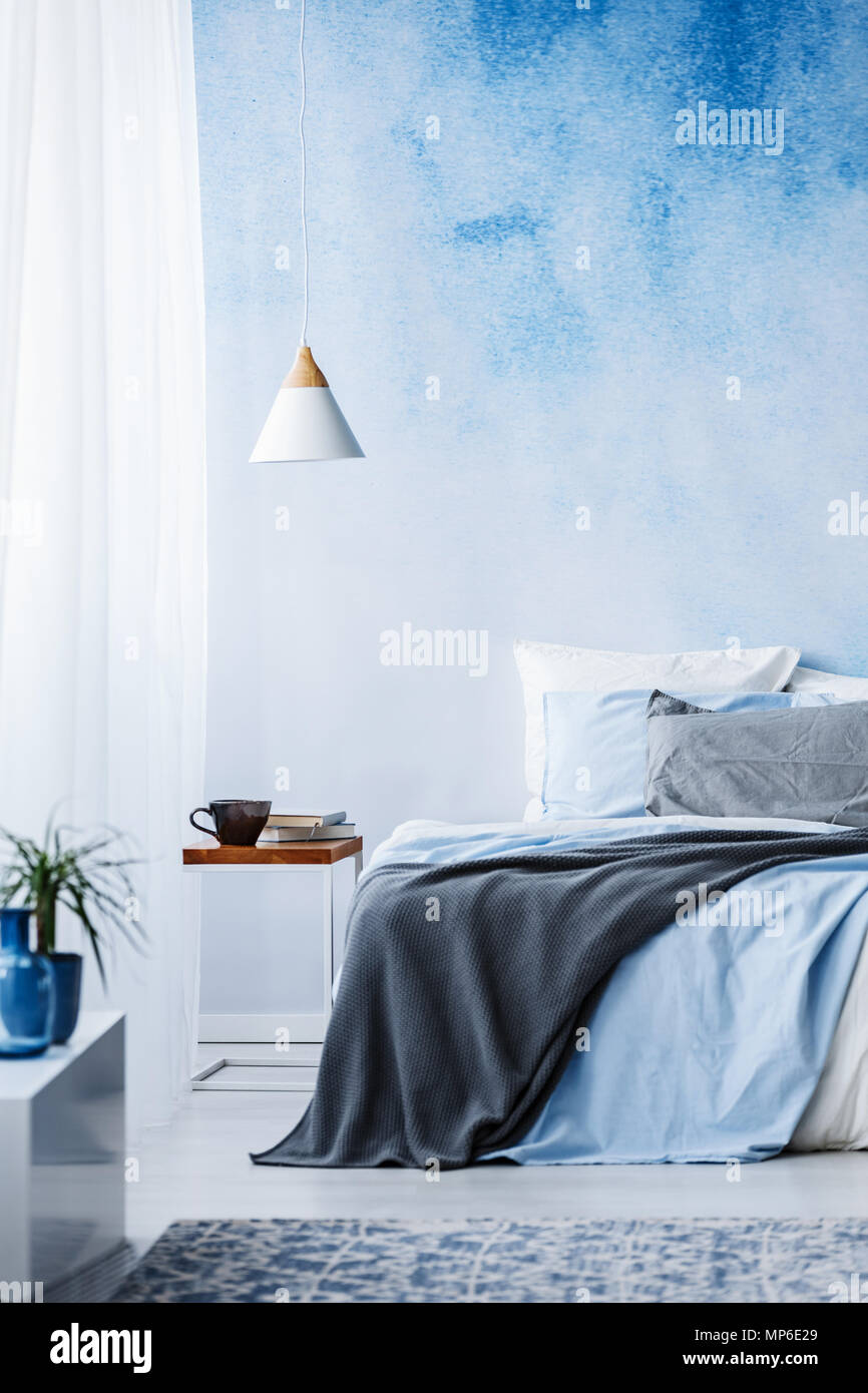 Blaue und graue Decke auf dem Bett gegen ombre Wand im Schlafzimmer Einrichtung mit weißen Lampe Stockfoto