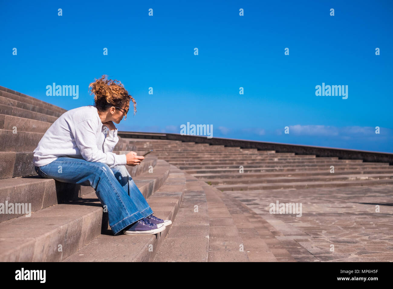 Nettes Mädchen Swirl braune Haare sitzen Sie in einer schönen städtischer Ort mit Sky Panorama mit zellularen Mobilfunk mit Freunden in Verbindung zu bleiben Stockfoto