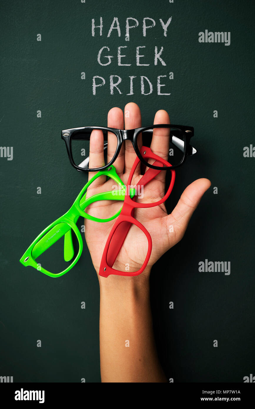 Einige Kunststoff - eingefaßte Brillen in verschiedenen Farben in der Hand des jungen Mannes und den Text gerne geek Pride gegen eine dunkelgrüne Oberfläche Stockfoto