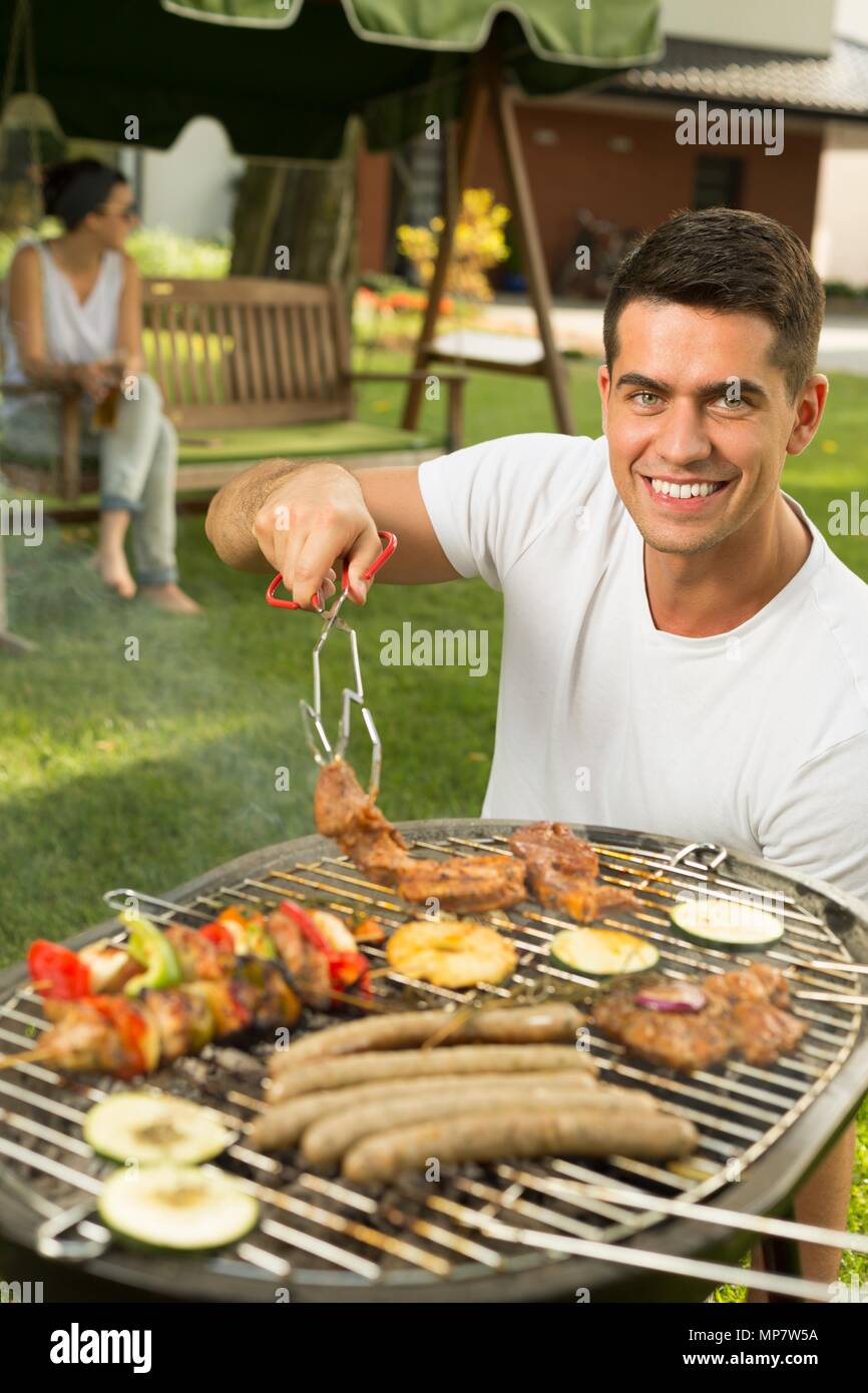 Der glückliche junge Mann tendenziell einen Grill Stockfoto