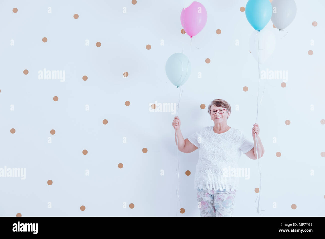 Lächelnde Großmutter halten bunte Luftballons gegen weiße Wand mit Gold dots Stockfoto