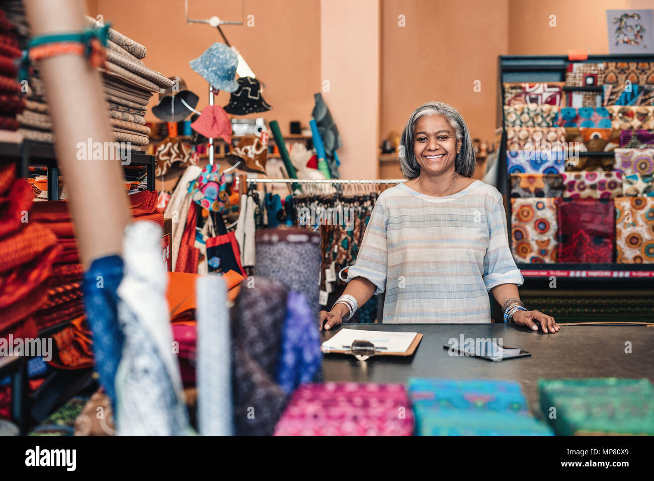 Lächelnd reife Frau in ihrem bunten Stoff shop arbeiten Stockfoto