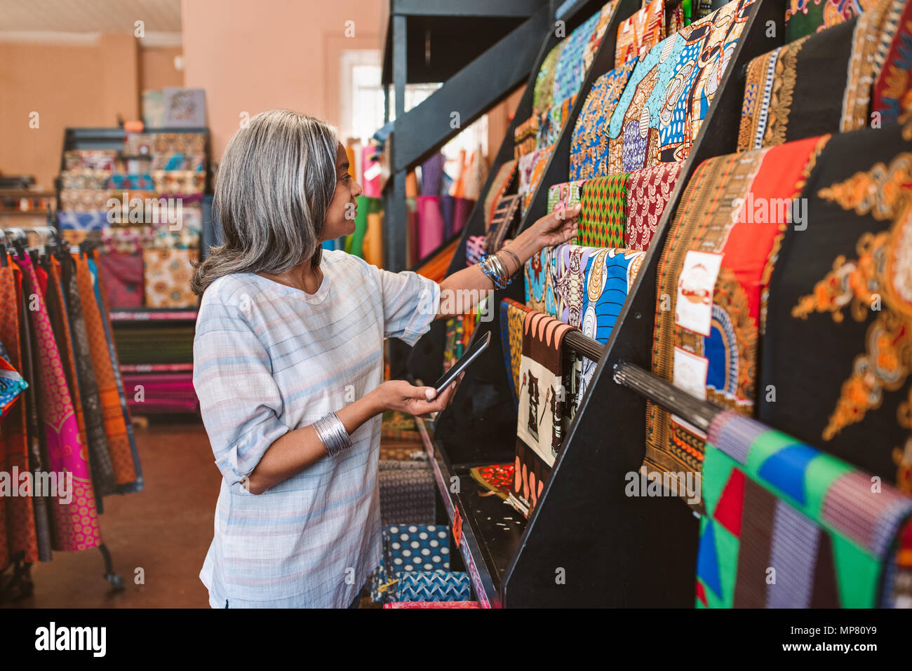 Reife Frau mit farbenfrohen Stoffen in Ihrem Shop suchen Stockfoto