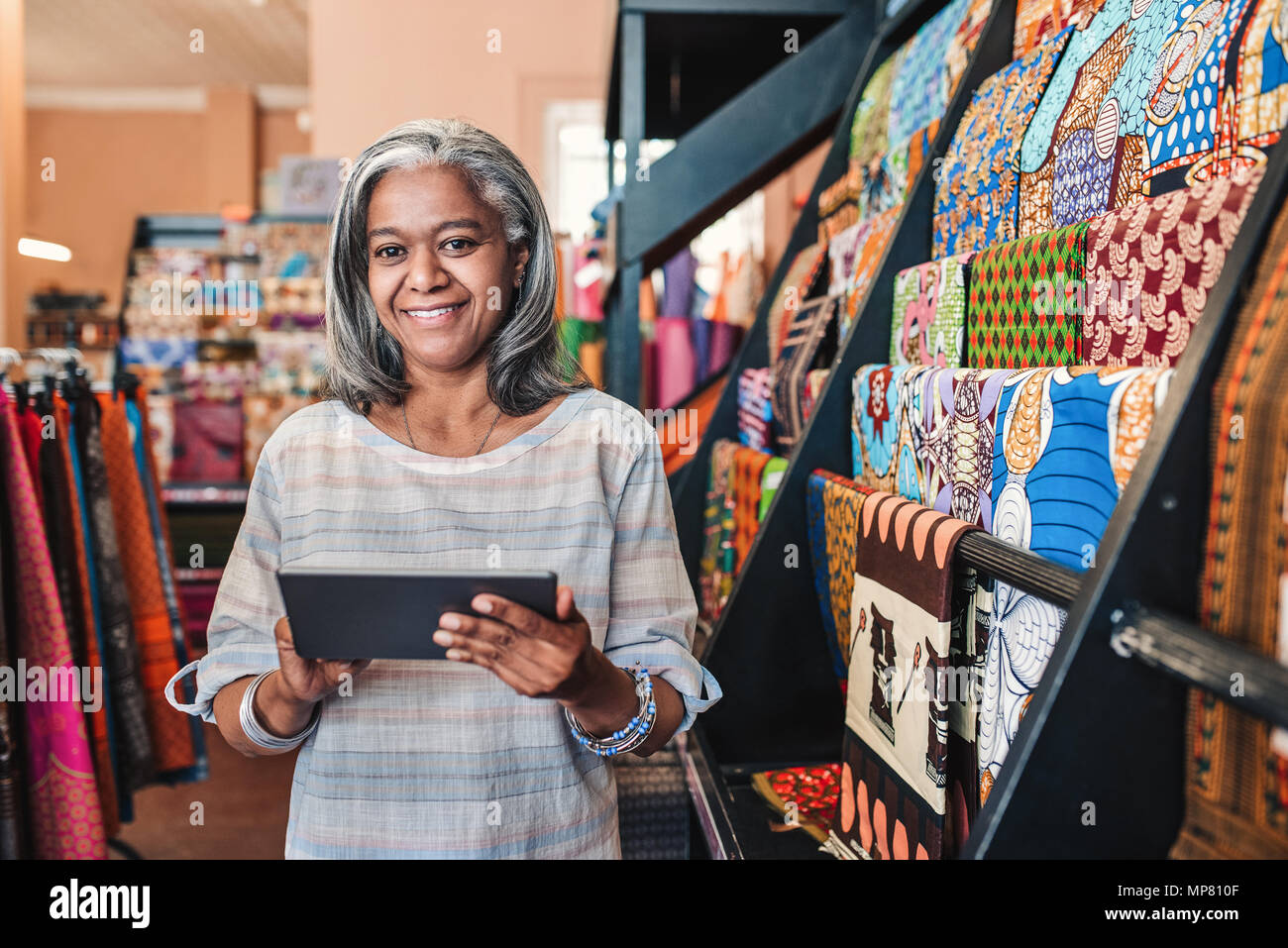 Lächelnde Frau mit einem digitalen Tablet in ihren Textilien Shop Stockfoto