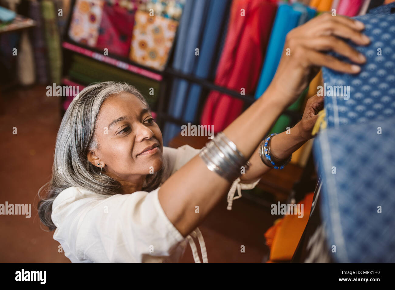 Lächelnde Frau mit Tuch Rollen in einem Stoff Shop suchen Stockfoto