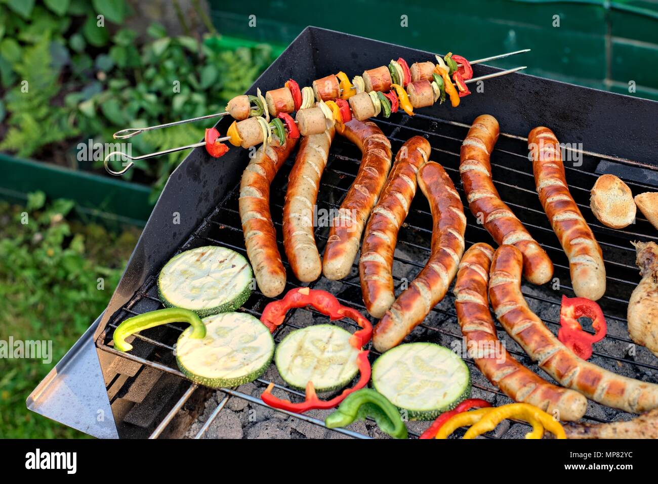 Leckeres Essen, Ernährung, kulinarischen und Grill Konzept: gegrillte Würstchen, Hähnchen Schenkel und Gemüse auf einem Grill. Stockfoto