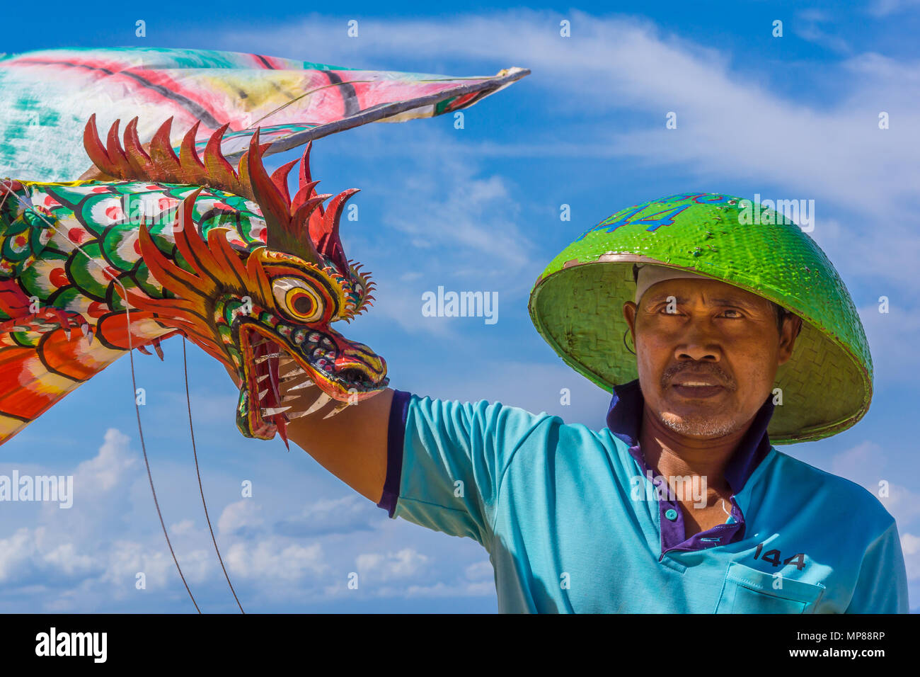 Ein indonesischer Mann in Grün Sonnenhut Holding einen großen roten Drachen mit einem schrecklichen Drachen Kopf, Sanur, Bali, Indonesien, 21. April 2018 Stockfoto