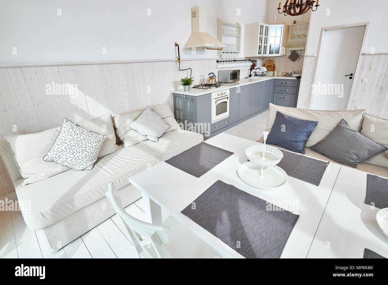 Wide Angle Shot der modernen offenen Wohnzimmer Einrichtung mit weißen Möbeln und grau Küche Zähler in minimalistischen skandinavischen Design durch Sonnenlicht beleuchtet Stockfoto