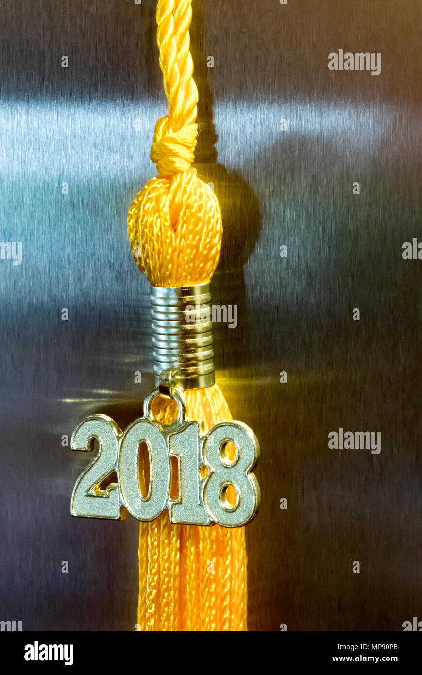 Klasse von 2018. Gold Quaste drop Graduierung kleid Zubehör und Andenken Charme gegen eine Metall Hintergrund. Iconic Symbol für den Erfolg eines Absolvent. Stockfoto