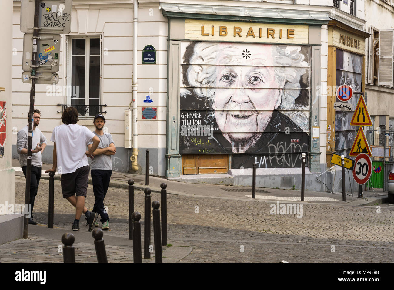 Drei Männer plaudern auf der Straße von Belleville Viertel in Paris, Frankreich, neben einer Wand mit Graffiti. Stockfoto