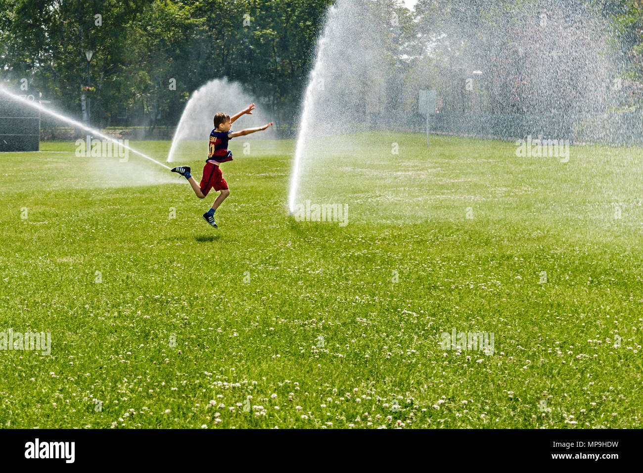 Ein kleiner Junge in einem FC Barcelona Fußball-Outfit auf dem Weg zu einer Kaskade von Wasser in den öffentlichen Park in Gliwice, Schlesischen Hochland, Polen springen. Stockfoto