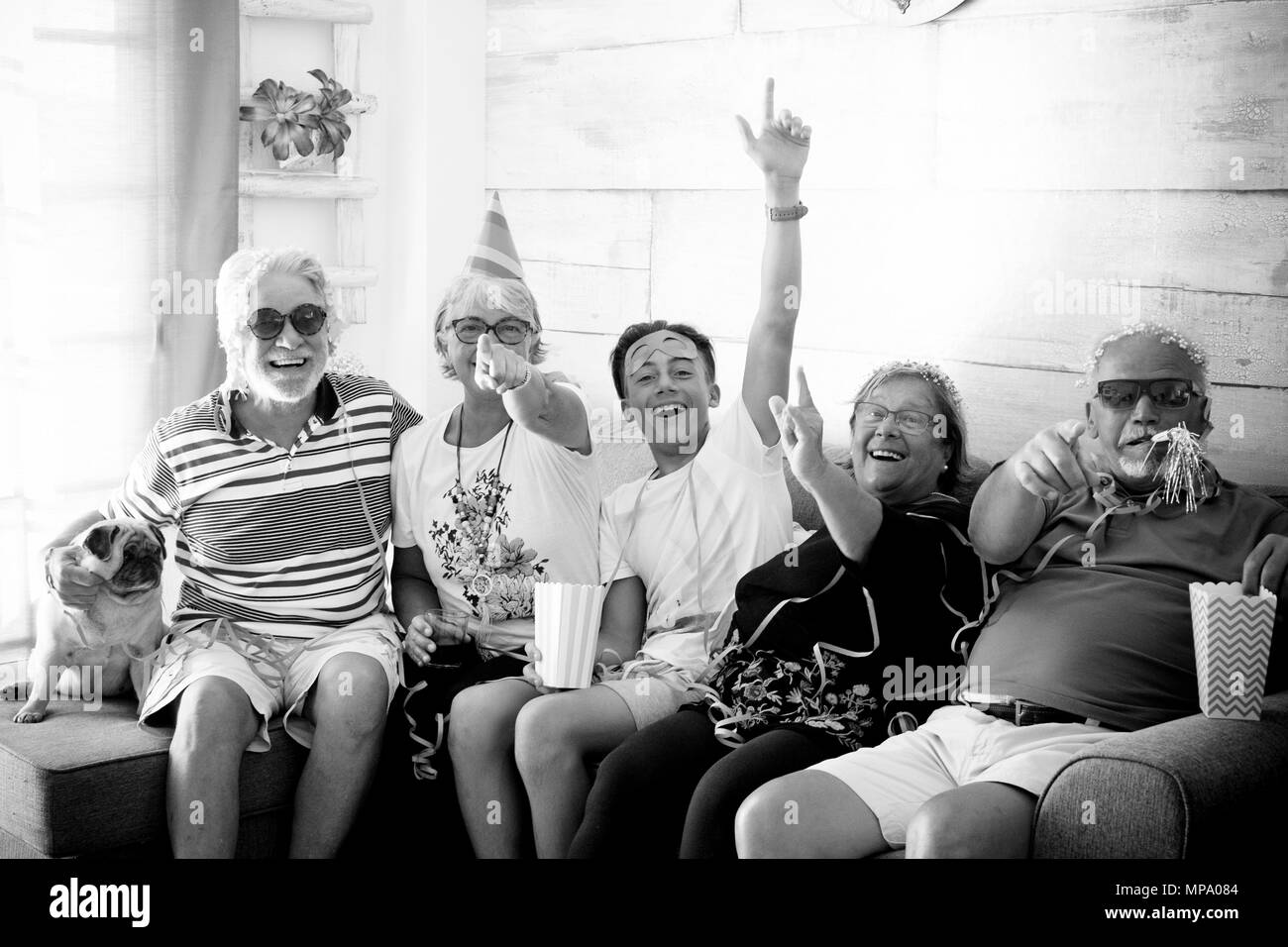4-köpfige Familie und Senioren mit weißem Haar und ein Jugendlicher in der Maske Lachen und Spielen auf dem Sofa sitzend feiern Stockfoto