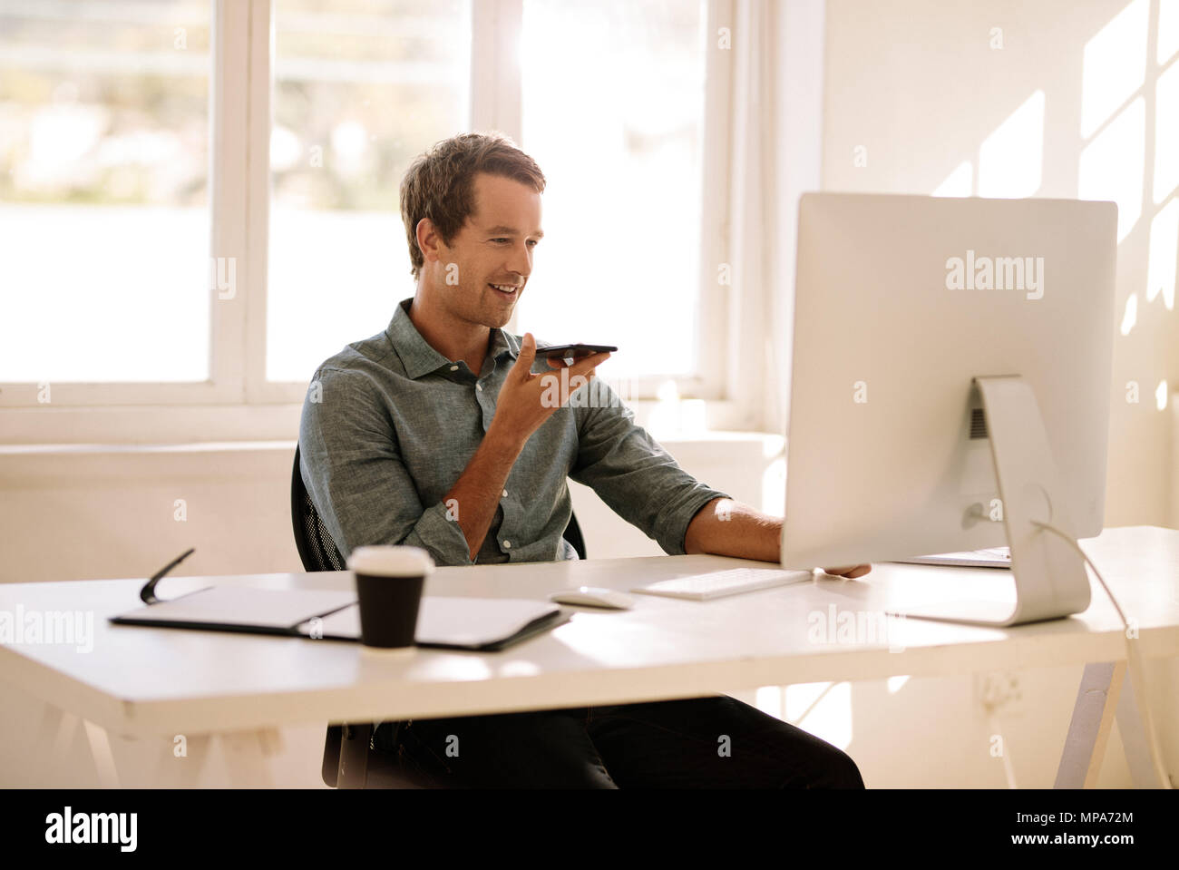 Mann mit Handy in der Hand und sprechen über die Lautsprecher am Computer suchen. Geschäftsmann aus dem Komfort von zu Hause aus arbeiten. Stockfoto