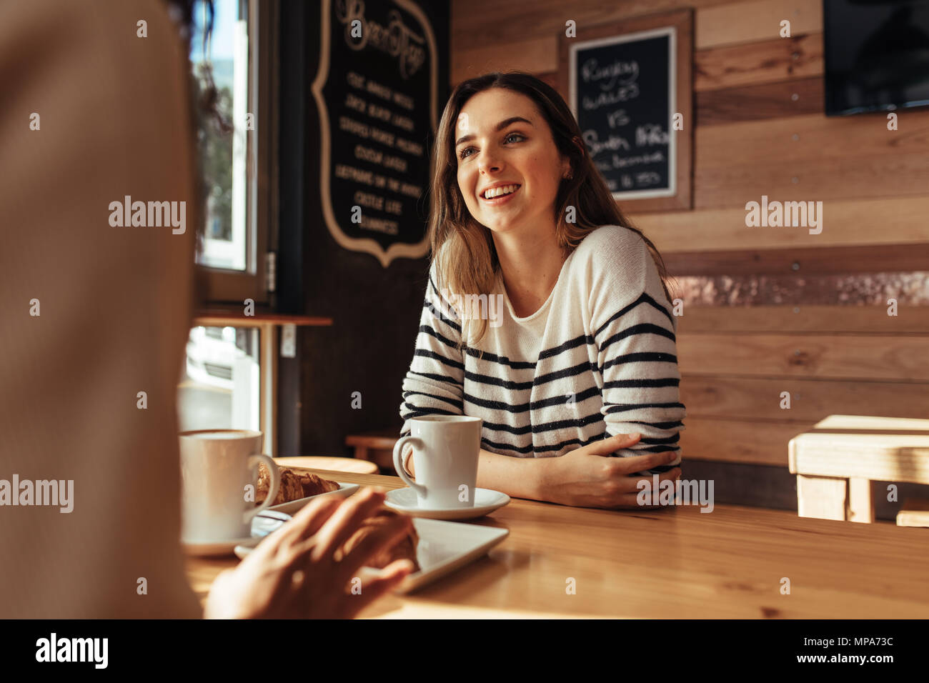 Lächelnde Frau in einem Restaurant sitzen im Gespräch mit ihrer Freundin. Freunde in einem Café mit Kaffee und Snacks auf den Tisch sitzen. Stockfoto