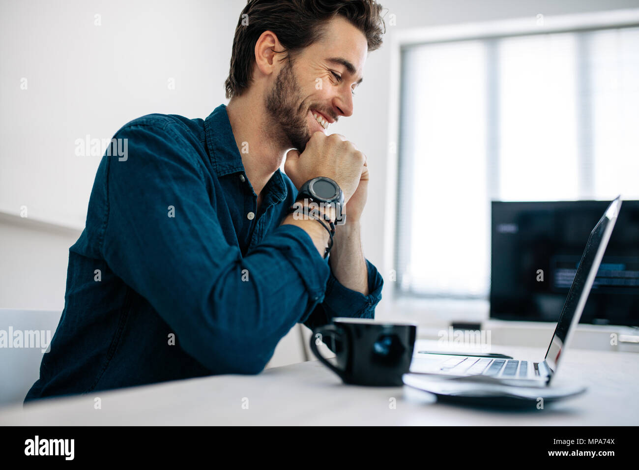 Software Entwickler sitzen vor dem Computer und Arbeiten im Büro. Lächelnd Mann am Laptop mit seinem Kinn auf die Hände mit einem Cof sitzen auf der Suche Stockfoto