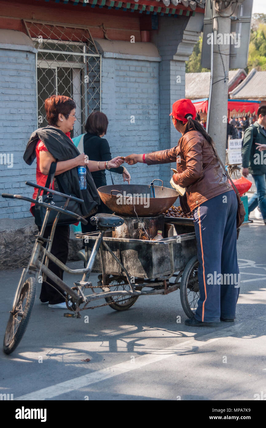 Peking, China - 29. April 2010: Street Scene, wo ambulante weiblich Straße Kaufmann verkauft geröstete Kastanien aus ihrem Dreirad. Kunde Stockfoto