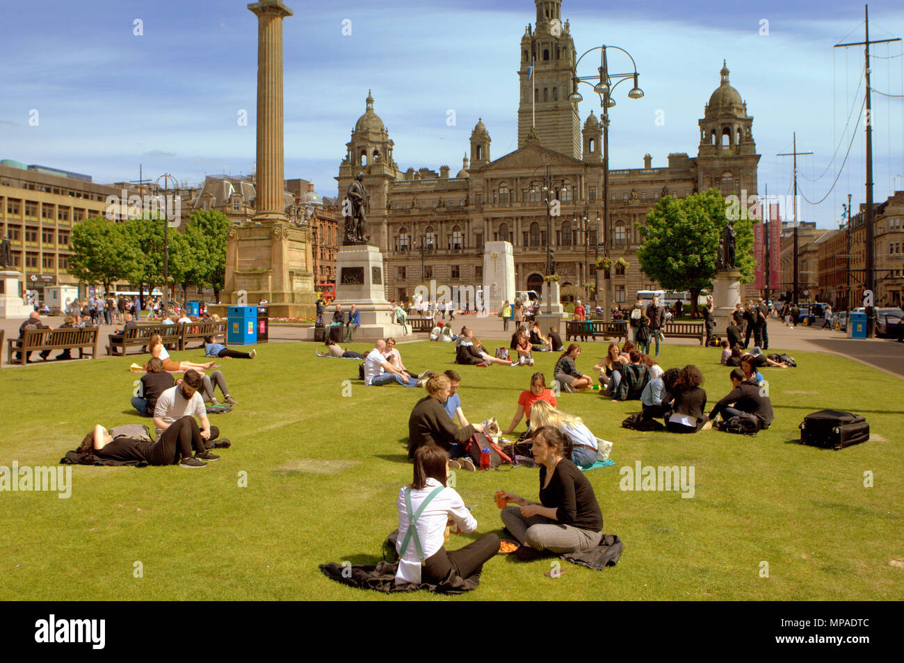 Einheimische und Touristen mit Büroangestellten auf ihr Mittagessen genießen Sie sitzen auf dem Gras auf dem George Square, Glasgow, Großbritannien Stockfoto