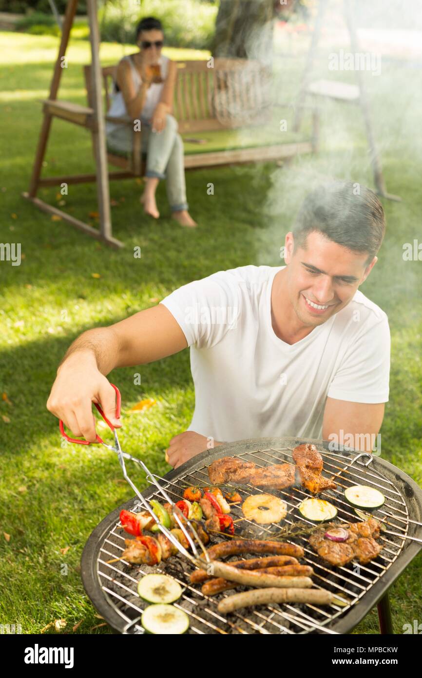 Junger Mann grillen Würstchen auf dem Grill Stockfoto