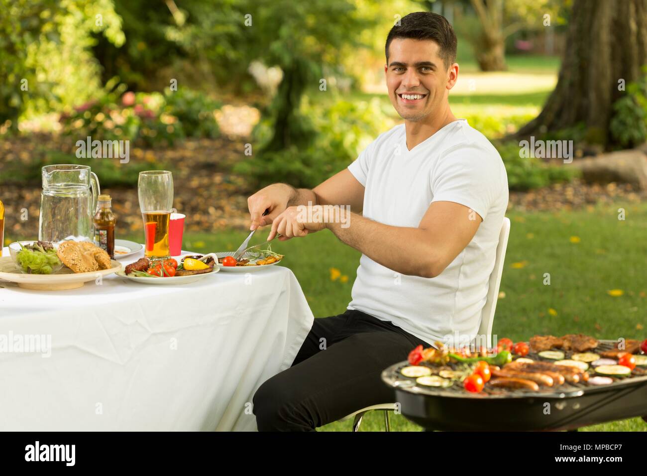 Der junge lächelnde Menschen Grillen in seinen Garten Stockfoto