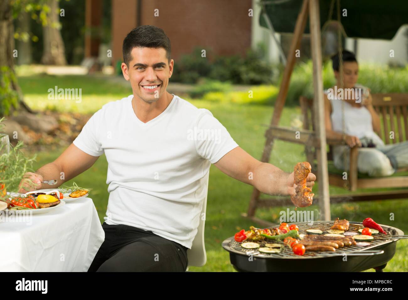 Junger Mann essen ein Stück saftiges Schweinefleisch für Abendessen vom Grill Stockfoto