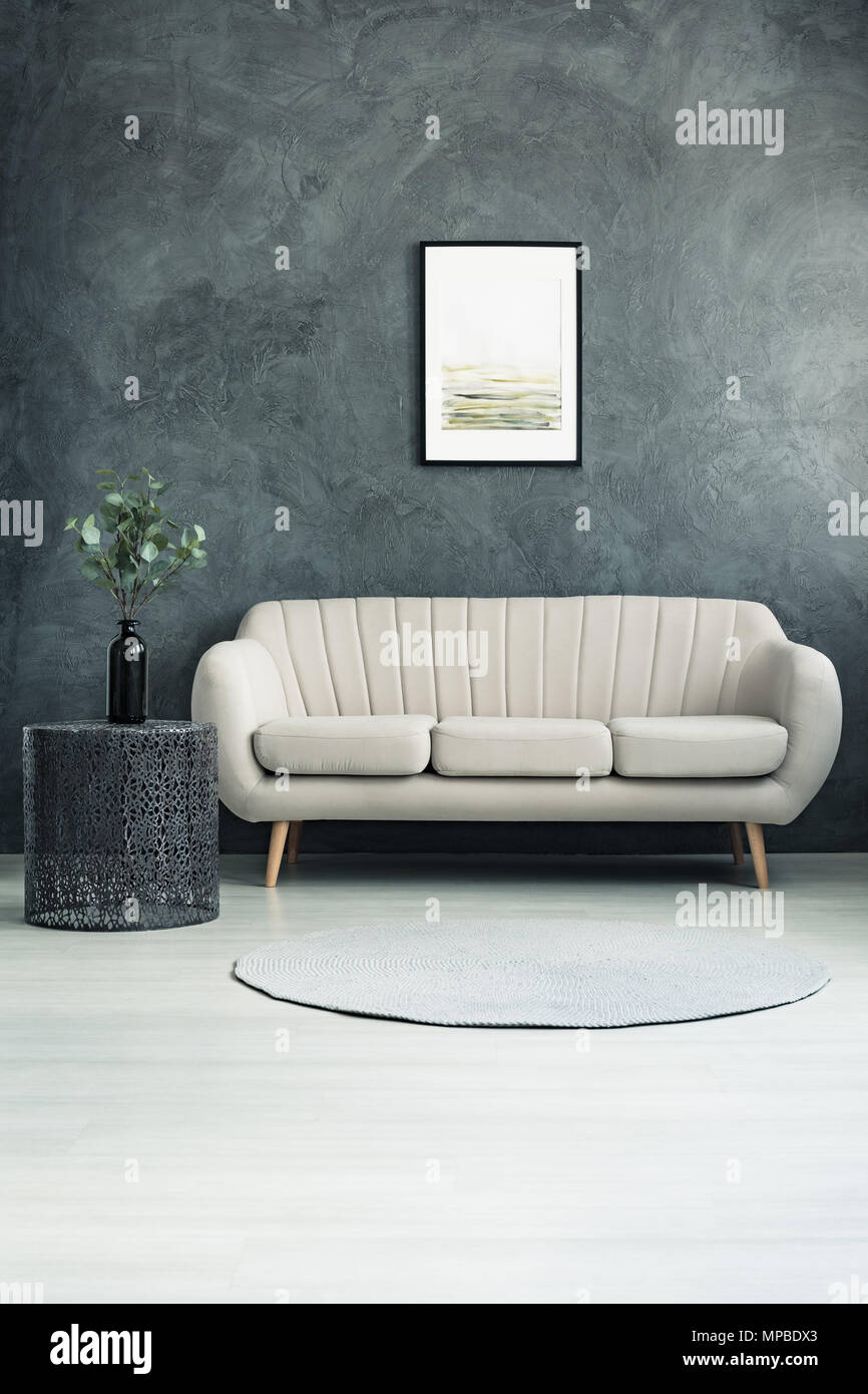 Helle Couch im Wohnzimmer mit Grau texturierte Wand und Zweige mit Blättern in einem Glas Vase auf Metall Tisch Stockfoto