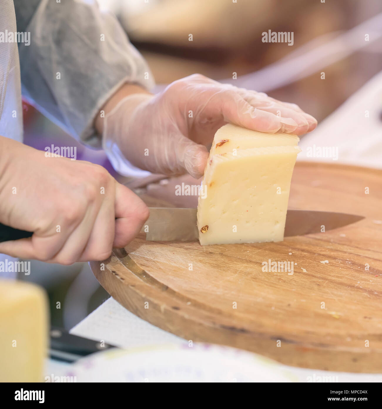 Verkäufer Schnitte und verkauft Käse, Käse, Köpfe auf Holz zu schneiden. Hände mit Messer schließen. Selektive konzentrieren. Gastronomische Milchprodukte, realen Szene, essen Markt Stockfoto