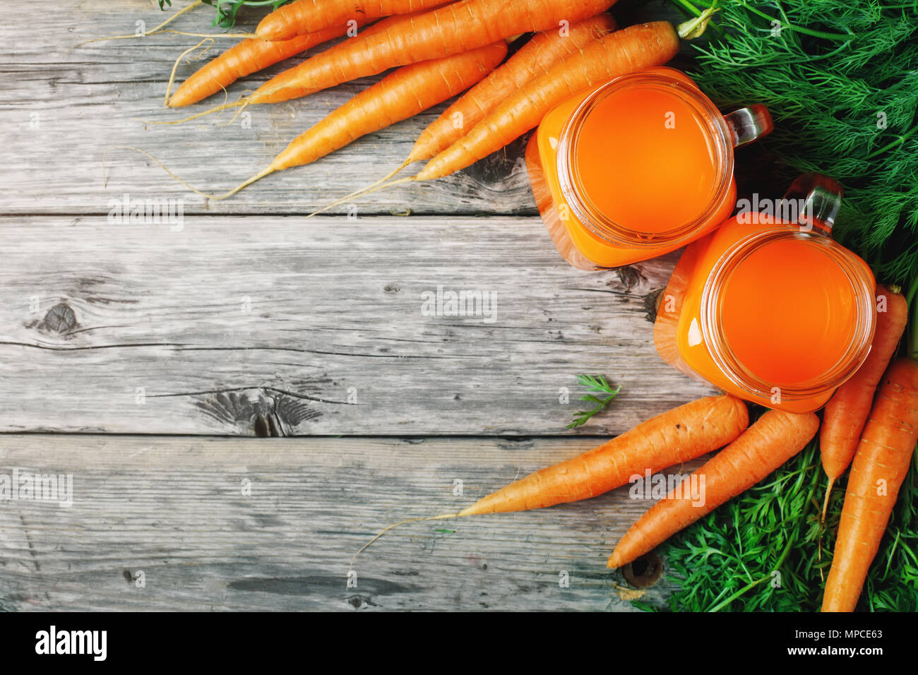 Frische Möhren und Karotten Saft auf hölzernen Tisch im Garten. Gemüse Vitamine Keratin. Natürliche organische Karotte liegt auf Holz- Hintergrund der Ansicht von oben Flach. Dorf auf dem Land im rustikalen Stil. Stockfoto