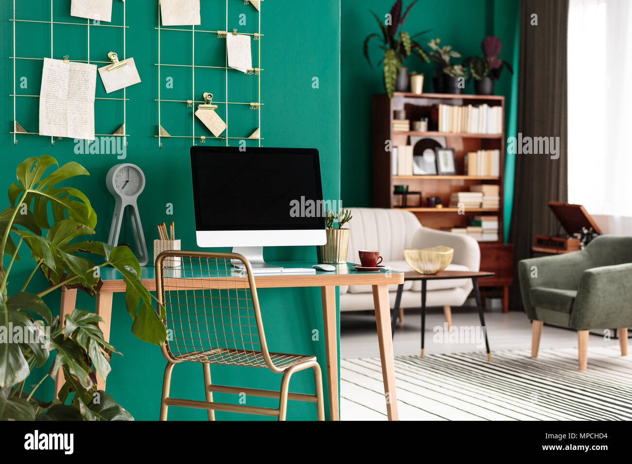 Gold Stuhl am Schreibtisch aus Holz mit Desktop-PC im Heimbüro Interieur mit Anlage gegen grüne Wand Stockfoto