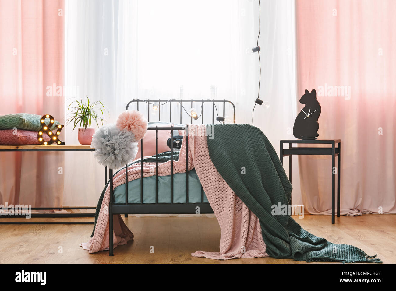 Vorderansicht eines Einzelbett mit Pompons, Wolldecken und pinkfarbenen Vorhängen in einem Schlafzimmer Innenraum Stockfoto