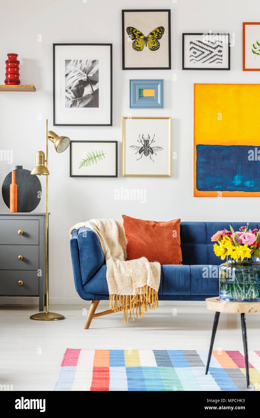 Decke und Kissen auf Marine blaue Couch in Weiß Wohnzimmer Einrichtung mit vielen Plakaten und gold Lampe Stockfoto