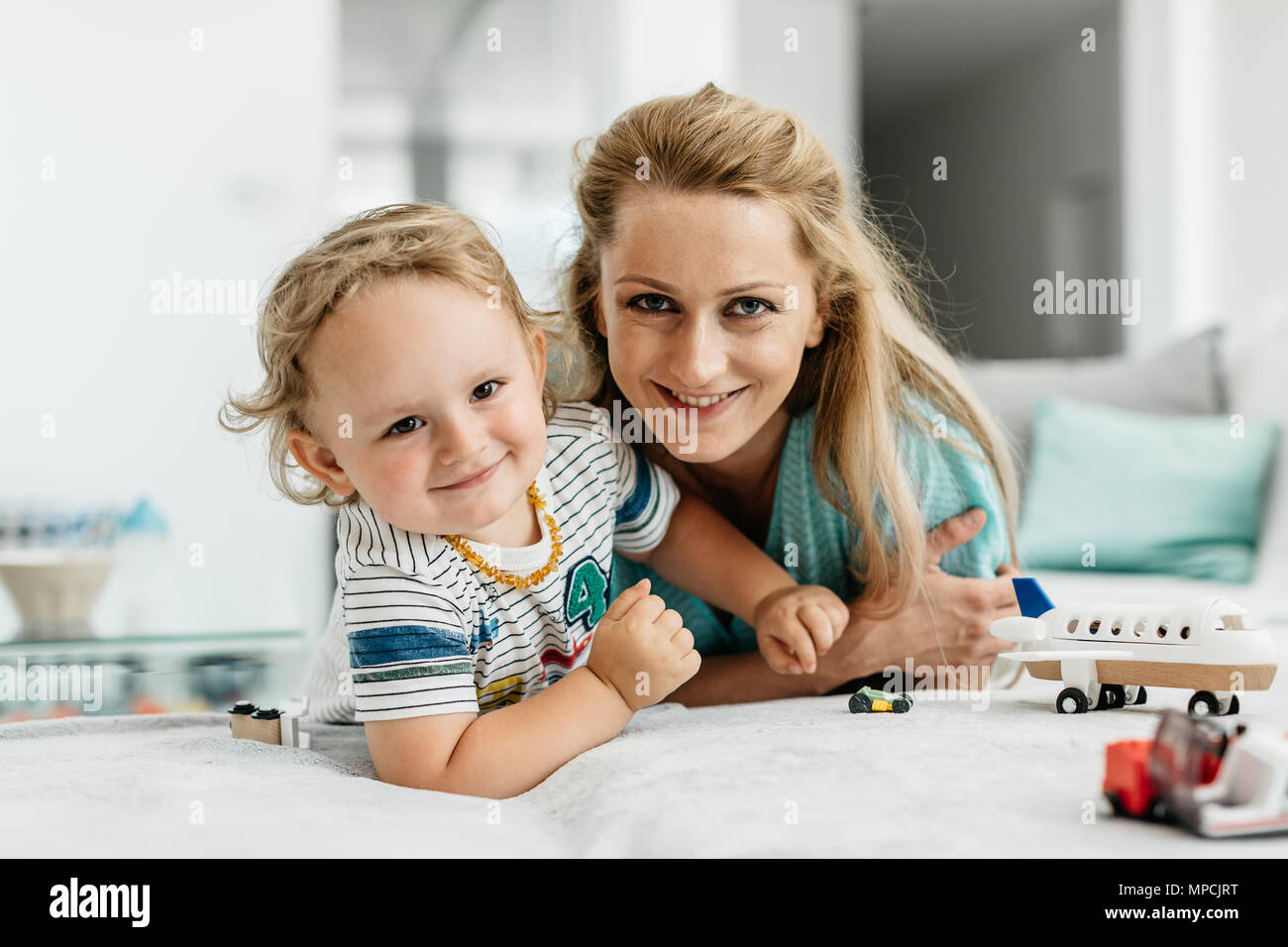 Eine glückliche Mutter und ihr Kind schaut in die Kamera. Das Porträt einer lächelnde Frau spielen zusammen mit ihren Toddler boy zu Hause. Stockfoto
