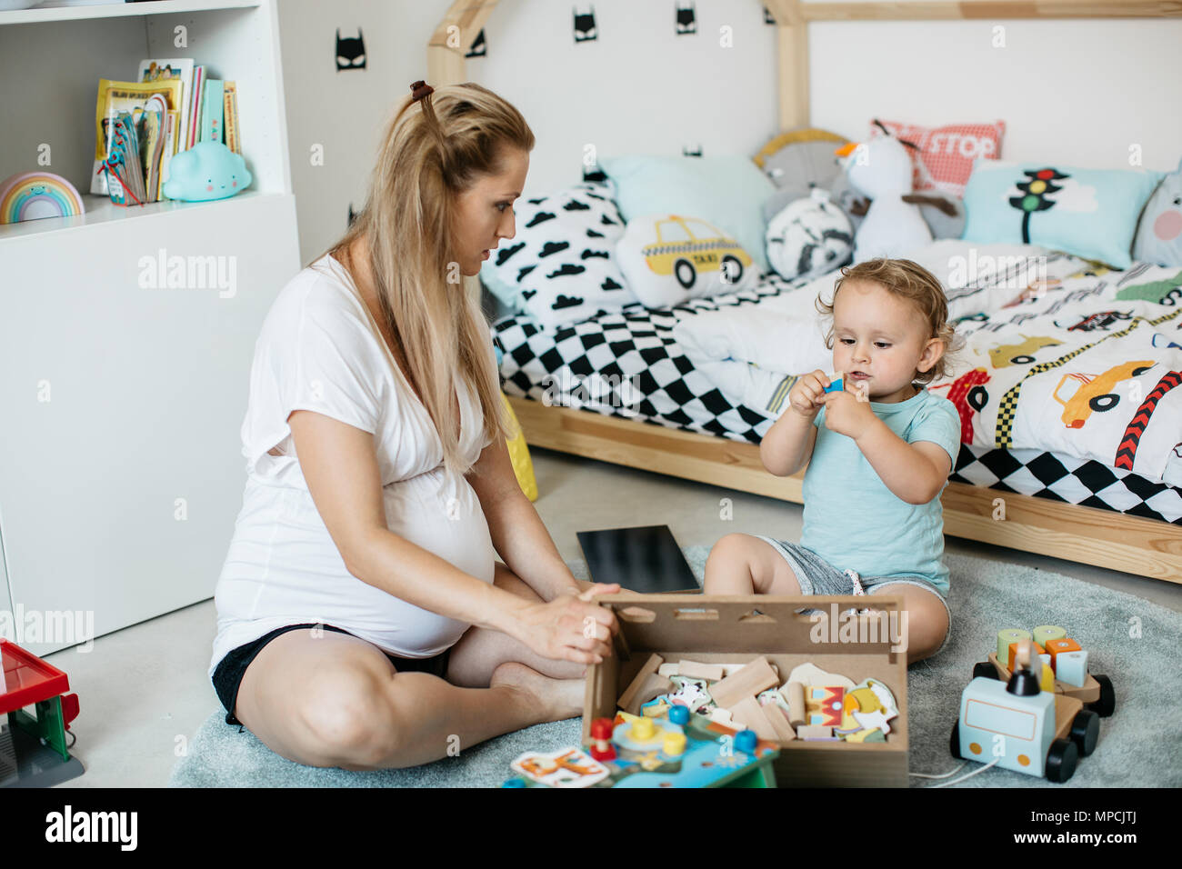 Eine schwangere Frau mit einem Kind in einem Spielzimmer. Eine Mutter und ihr Kind Junge Zeit miteinander zu verbringen und Lernen mit Holzspielzeug. Stockfoto