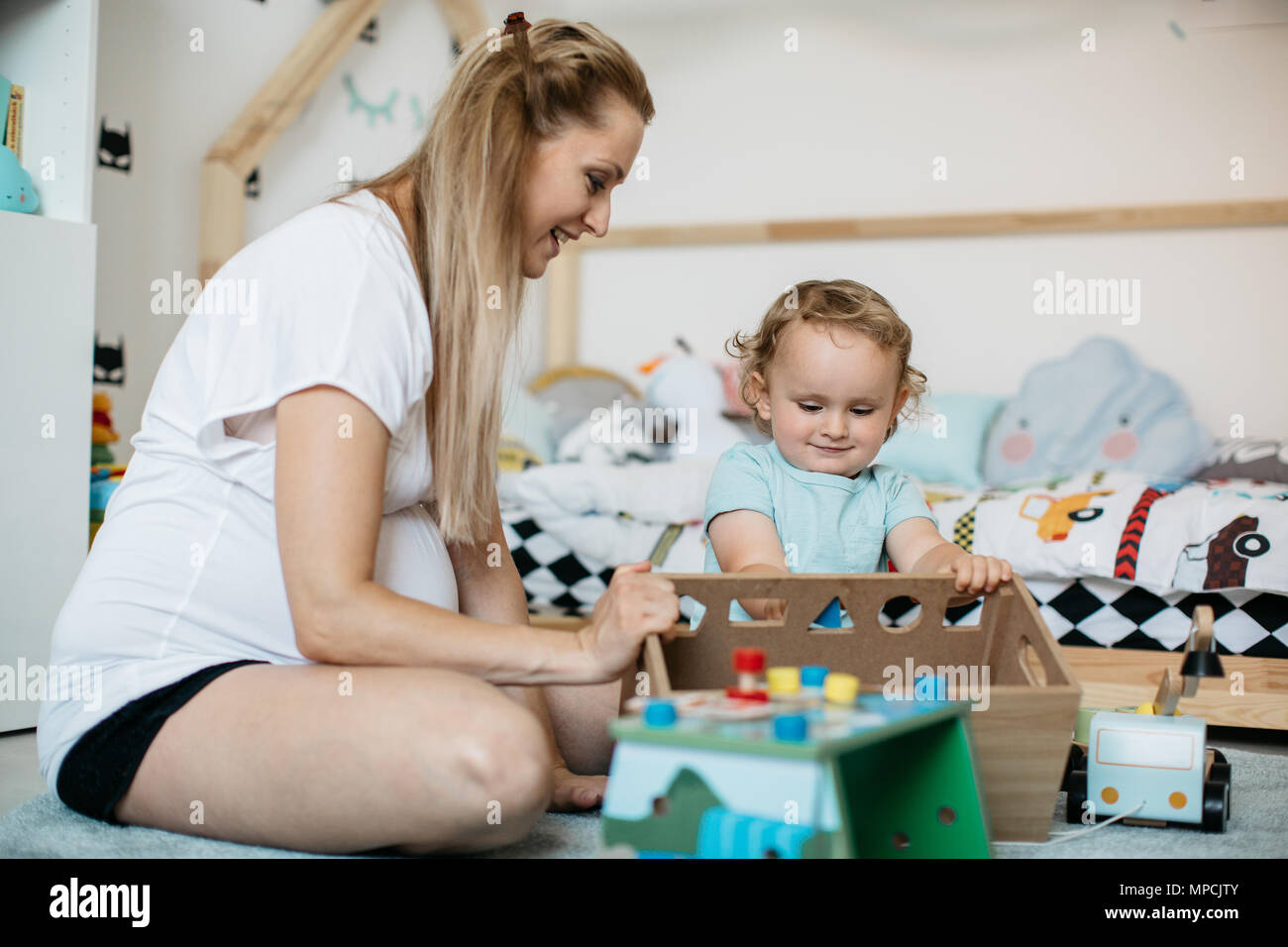 Ein Porträt eines lächelnden Mutter lehre Formen zu ihren Toddler boy zu Hause. Eine glückliche Mutter und ihr Sohn das Spiel mit geometrischen Formen in ein Spielzimmer. Stockfoto