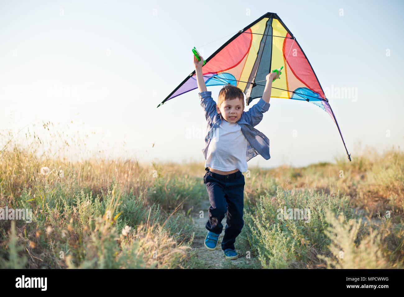 Happy cute kid laufen im Freien mit bunten Drachen über Kopf in den Sommer Feld Stockfoto