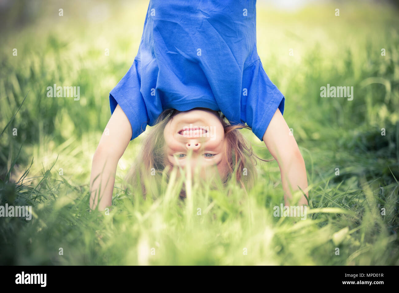 Glückliche kleine Mädchen stehen auf dem Kopf stehend auf dem Rasen im Sommerpark Stockfoto