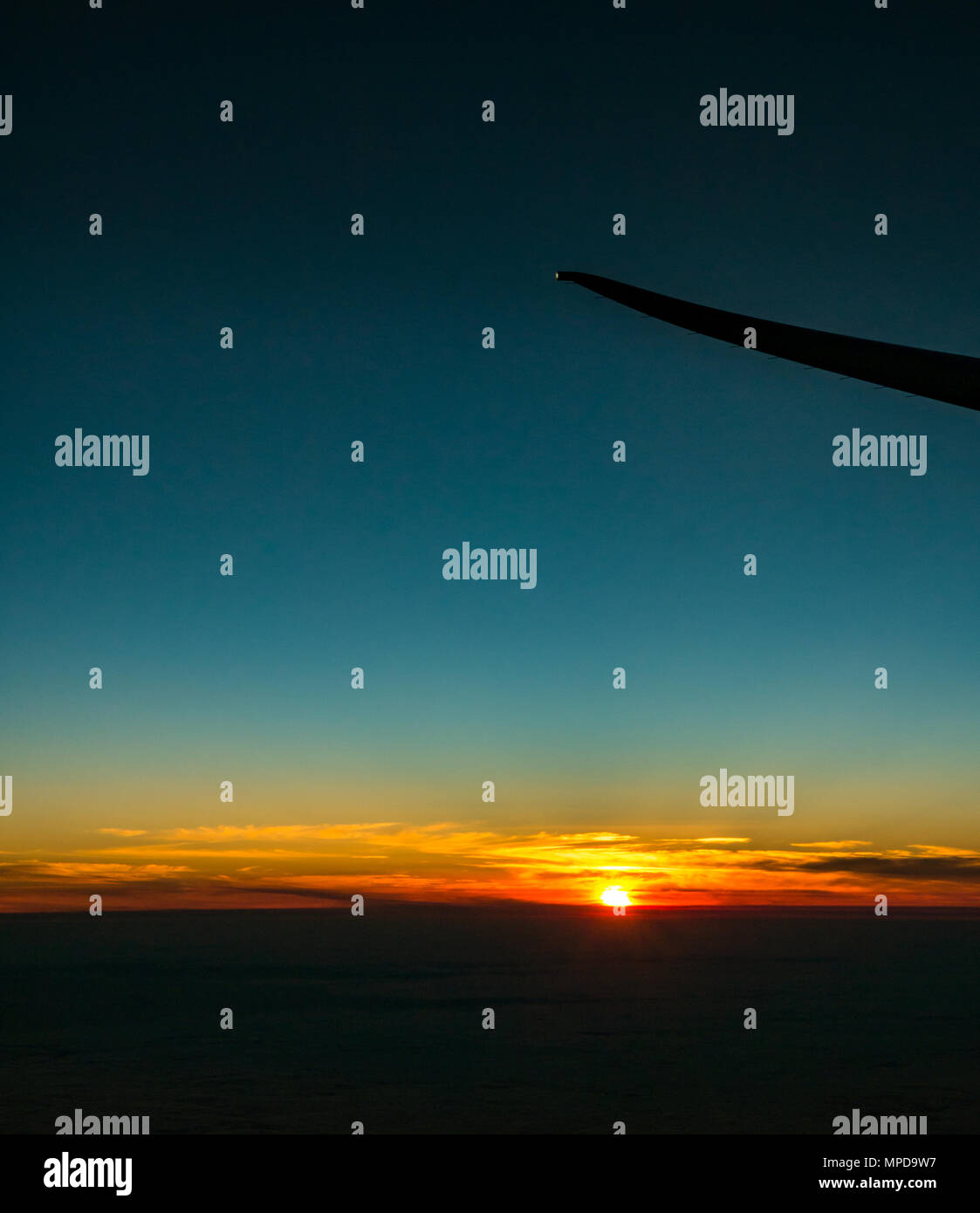 Orange Sonnenuntergang mit klaren blauen Himmel und Horizont, aus dem Flugzeug Fenster, mit einem Flugzeugflügel tipp Silhouette, von Heathro, London, UK Stockfoto