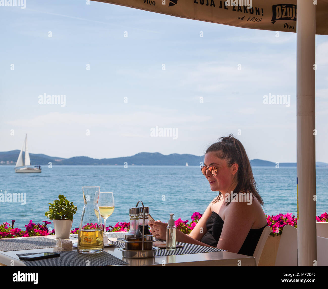 Junge Frau Mädchen an einen Tisch im Restaurant außerhalb mit einem Glas können Sie über Ihr Mobiltelefon an der Adria Resort von Zadar Kroatien Wein sitzen Stockfoto
