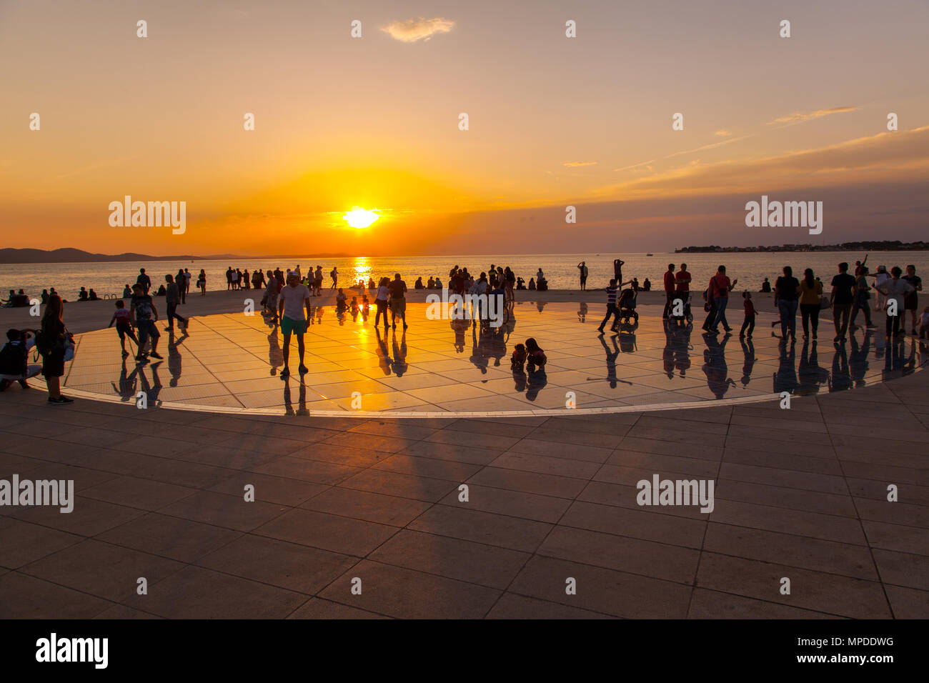 Urlaubern und Touristen bewundern eine glorreiche orange Sonnenuntergang vom photovolt Installation, das Denkmal für die Sonne im Hafen von Zadar Kroatien Stockfoto